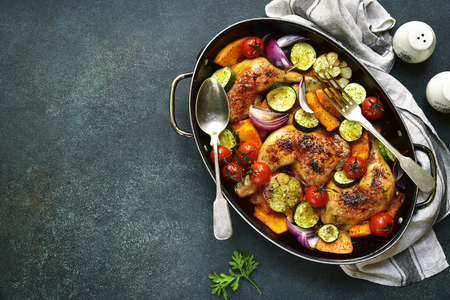 Chicken legs roasted with vegetables in a skillet pan over dark slate,stone or concrete background.Top view.の写真素材