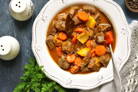 Meat stewed with vegetables in tomato sauce (hungarian gouliash) in a vintage plate over dark blue slate,stone or concrete background.Top view .の写真素材