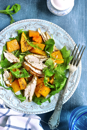 Pumpkin salad with chicken and arugula on a vintage plate over dark blue slate,stone or concrete background.Top view.の写真素材
