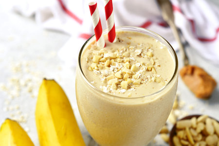 Banana peanut butter smoothie with oats and cinnamon in a glass on a light slate,stone or concrete...