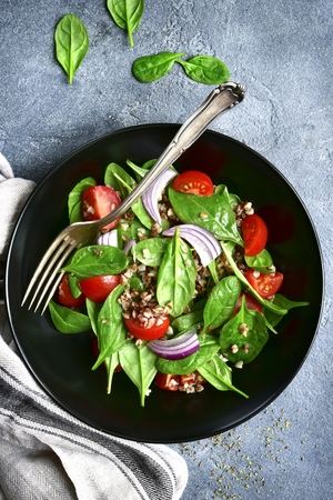 Buckwheat salad with spinach, cherry tomato and red onion in a black bowl over dark grey slate, stone or concrete background.Top view with copy space.の写真素材