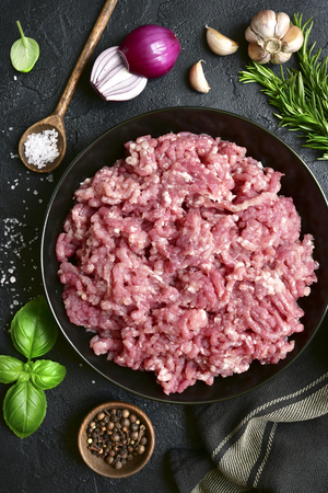 Homemade minced meat in a black bowl over dark slate or stone background with ingredients for making.Top view with copy space.の写真素材