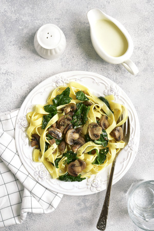 Tagliatelle pasta with spinach and mushrooms served with cream sauce beachamel on a white plate over light slate, stone or concrete background.Top view.の写真素材