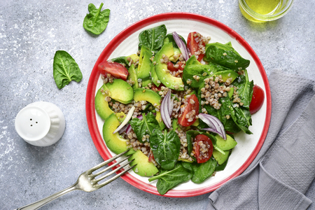 Vegetable sald with avocado, baby spinach, tomato and buckwheat on a vintage plate over light grey slate, stone or concrete background.Top view.の写真素材