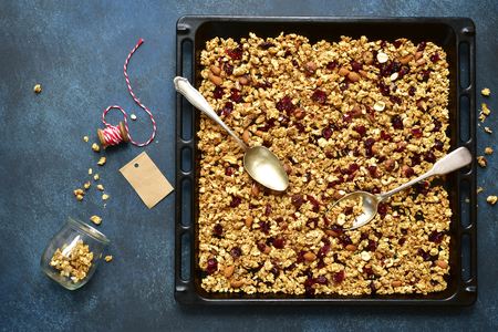 Homemade granola from mix of cereals (barley, oat, rye, bran) with dry fruits, nuts and seeds on a black metal tray- concept of healthy breakfast.Top view with copy space.の写真素材