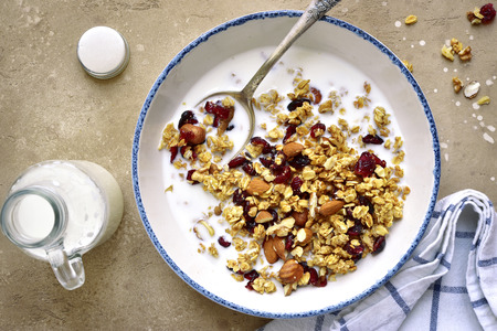 Homemade granola with milk for a breakfast in a vintage bowl over light beige slate, stone or concrete background.Top view.の写真素材