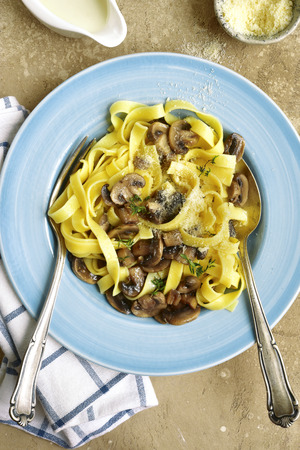 Pasta tagliatelle with mushrooms, parmesan and thyme in a cream sauce on a blue plate over beige slate, stone or concrete background.Top view.の写真素材