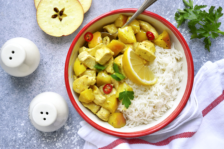 Chicken fillet stewed with red apples and curry served with boiled rice in a vintage bowl over light slate, stone or concrete background.Top view.の写真素材