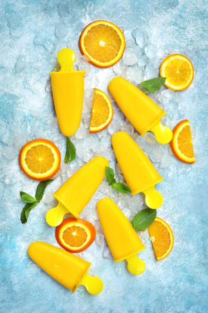 Vegan orange ice cream pop on an ice cubes over light blue slate, stone or concrete background.Top view with copy space.の写真素材