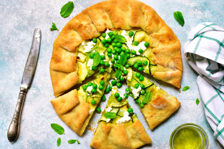 Delicious summer galette with zucchini, feta cheese, green pea and mint on a light slate, stone or concrete background.Top view.の写真素材