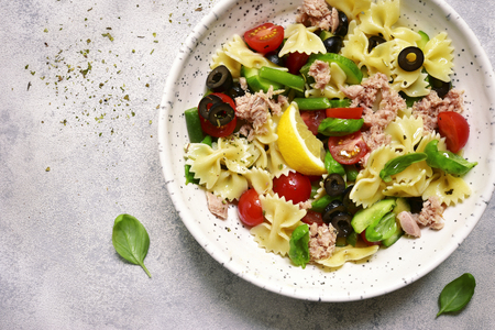 Pasta salad with tuna and vegetables ( cherry tomato, cucumber, green bean and black olives ) in a white bowl over light slate, stone or concrete background. Top view.の写真素材