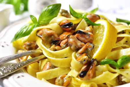 Tagliatelle pasta with mussels in a cream sauce on a white plate on a light slate, stone or concrete background.の写真素材