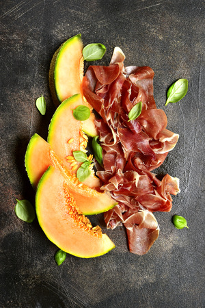 Sliced melon and jamon or prosciutto with bottle of red wine on a dark salte, stone or concrete background.Top view.の写真素材