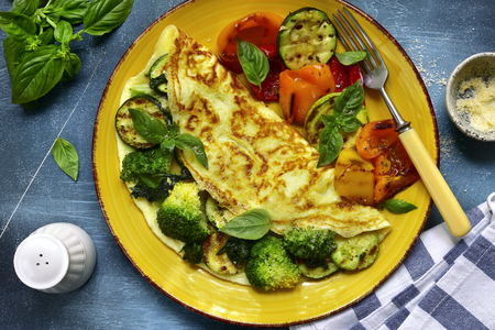 Omelette stuffed with green vegetables (broccoli, zucchini, spinach) garnished with grilled bell pepeer on a yellow plate over dark blue slate, stone or concrete background.Top view.の写真素材