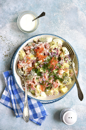 New potato salad with salted salmon, pickled cucumber, egg, capers and red onion in a vintage bowl over light blue slate, stone or concrete background.Top view.の写真素材