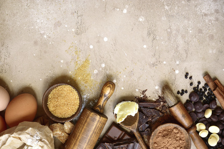 Ingredients for festive baking : flour, brown sugar, eggs, chocolate slices and drops, cocoa, butter and cinnamon on a beige slate, stone or concrete background.Top view with copy space.の写真素材