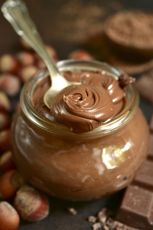 Homemade chocolate hazelnut spread in a vintage jar on a dark brown slate, stone or concrete background.の写真素材