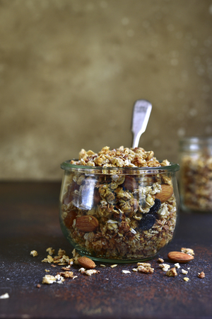 Homemade granola from mix of cereals (barley, oat, rye, bran) with dry fruits, nuts and seeds in a vintage jar on a  slate or concrete table- concept of healthy breakfast.の写真素材