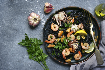 Black seafood spaghetti on a dark plate over grey slate, stone or concrete background.Top view with copy space.の写真素材