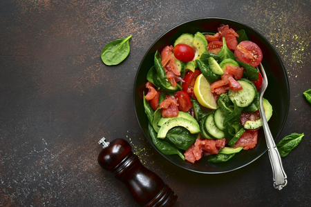 Fresh vegetable salad with salted salmon in a black plate over dark slate, stone or concrete background.Top view with copy space.の写真素材