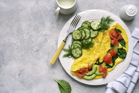 Omelette stuffed with spinach, cheese, avocado and salted salmon on a white plate over light slate, stone or concrete background.Top view with copy space.の写真素材