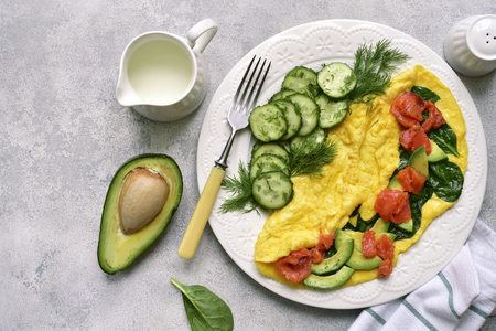 Omelette stuffed with spinach, cheese, avocado and salted salmon on a white plate over light slate, stone or concrete background.Top view with copy space.の写真素材