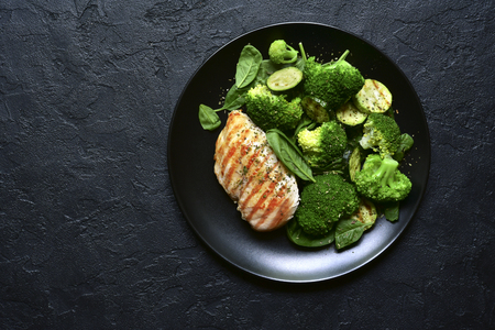 Grilled chicken fillet with green vegetable salad on a black slate, stone or concrete background.Top view with copy space.の写真素材