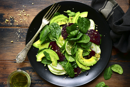Vegetable salad with avocado, apple, beetroot, spinach and walnut on a black plate over dark rustic wooden background.Top view with copy space.の写真素材
