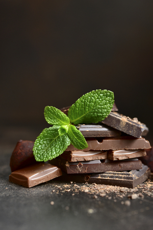 Chocolate slices with fresh mint leaves on a dark slate, stone or concrete background.の写真素材
