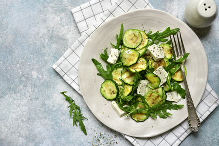 Grilled zucchini salad with feta cheese and arugula on a plate over light blue slate, stone or concrete background.Top view with copy space.の写真素材