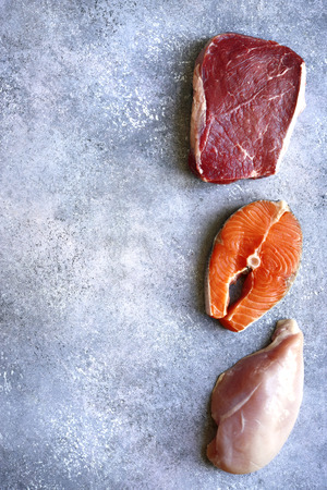 Raw marbled meat, red fish and chicken breast on a light grey slate, stone or concrete background.の写真素材