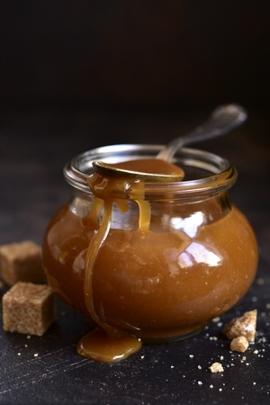 Homemade salted caramel sauce in a vintage jar on a dark slate, stone or concrete background.の写真素材