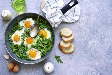 Healthy vegetarian breakfast : fried eggs and asparagus bean in a skillet over light grey slate, stone or concrete backgrond.Top view.の写真素材