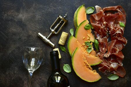 Sliced melon and jamon or prosciutto with bottle of red wine on a dark salte, stone or concrete background.Top view with copy space.の写真素材