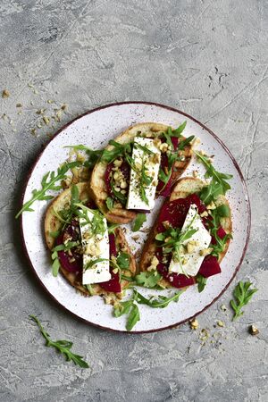 Healthy toasts with beetroot, feta cheese, nuts and arugula on a plate over grey slate, stone or concrete background.Top view with copy space.の写真素材