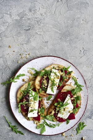Healthy toasts with beetroot, feta cheese, nuts and arugula on a plate over grey slate, stone or concrete background.Top view with copy space.の写真素材
