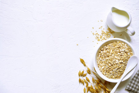 Raw organic oat flakes with milk in a white bowl over light slate, stone or concrete background -...