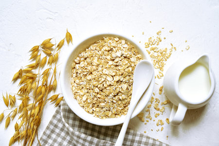 Raw organic oat flakes with milk in a white bowl over light slate, stone or concrete background -...