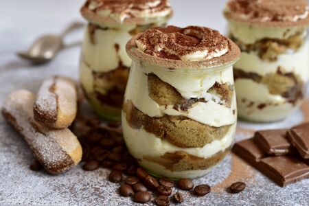 Traditional italian creamy dessert with mascarpone, biscuit and coffee in a vintage jars on a light slate, stone or concrete background.の写真素材