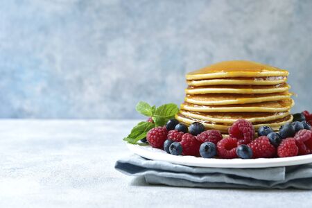 Homemade hot pancakes with maple syrup and fresh berries on a plate on a light blue slate, stone or concrete background.の写真素材
