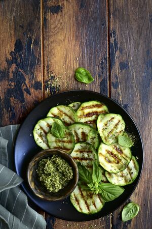 Grilled zucchini slices with basil pesto on a black plate over dark wooden background.Top view with copy space.の写真素材