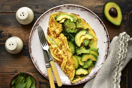 Omelette stuffed with green vegetables : broccoli, avocado and baby spinach on a plate on a dark wooden background.Top view with copy space.の写真素材