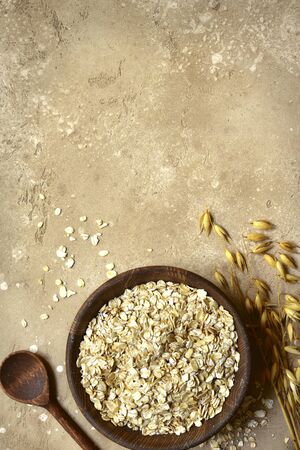 Raw organic oat flakes in a wooden bowl on a light slate, stone or concrete background. Top view with copy space.の写真素材