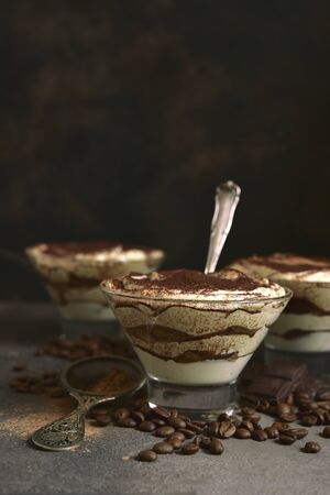 Tiramisu - traditional italian dessert from mascarpone cheese and biscuit in a glasses on a dark slate, stone or concrete background. No baked chessecake.の写真素材