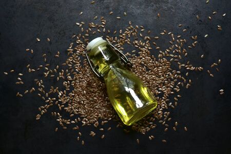Linseed oil in a bottle and flax seed on a dark metal background. Top view with copy space.の写真素材
