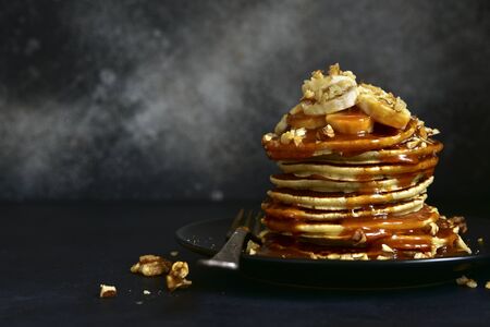 Hot banana pancakes with caramel sauce and walnuts on a black plate on a dark slate, stone or concrete background.の写真素材