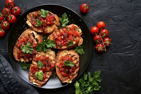 Grilled toasts with tomato salsa on a black plate on a dark slate, stone or concrete background. Top view with copy space.の写真素材