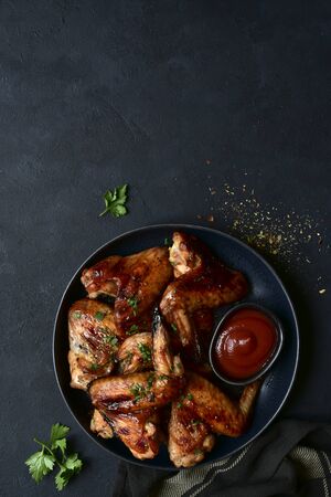 Grilled spicy chicken wings with ketchup on a black plate on a dark slate, stone or concrete background. Top view with copy space.の写真素材