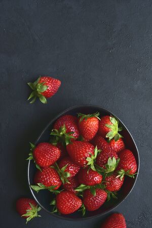 Fresh ripe organic strawberry in a white bowl on a dark slate, stone or concrete background. Top view with copy space.の写真素材