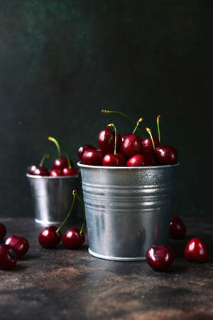 Fresh ripe organic cherry in a metal bucket on a dark slate, stone or concrete background.の写真素材